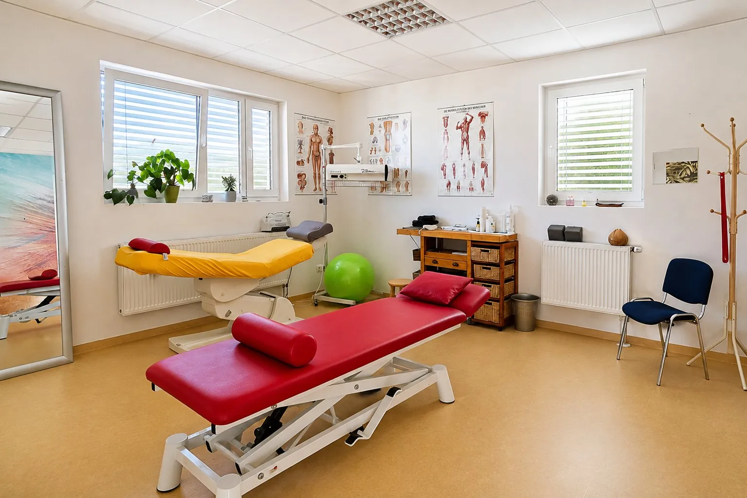 Zweiter Behandlungsraum mit Therapieliege, Spiegel und anatomischen Tafeln