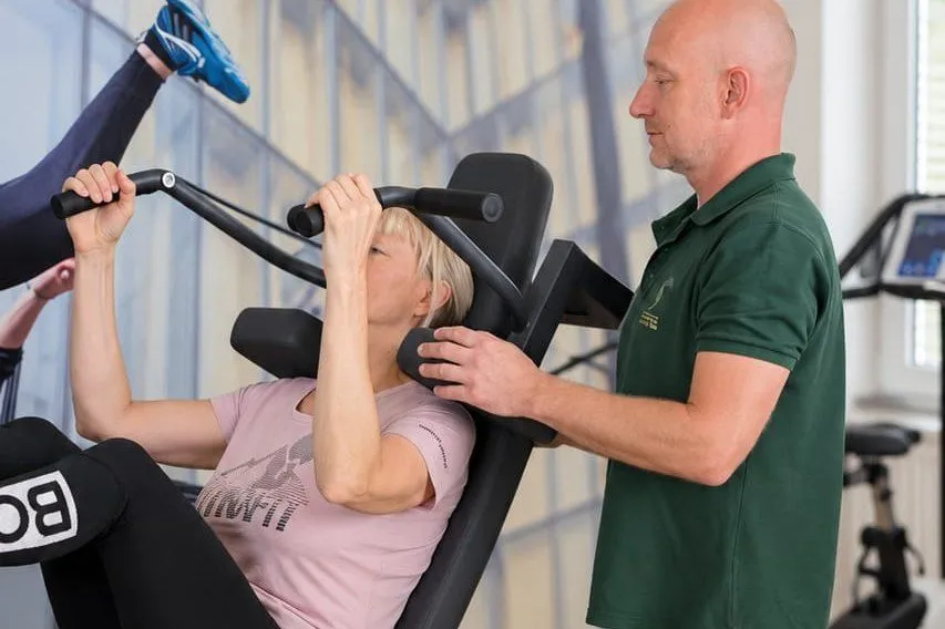 Therapeut begleitet eine Patientin beim Training an der Beinpresse