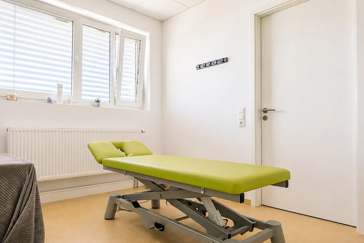 Heller Behandlungsraum der Praxis mit Therapieliege am Fenster